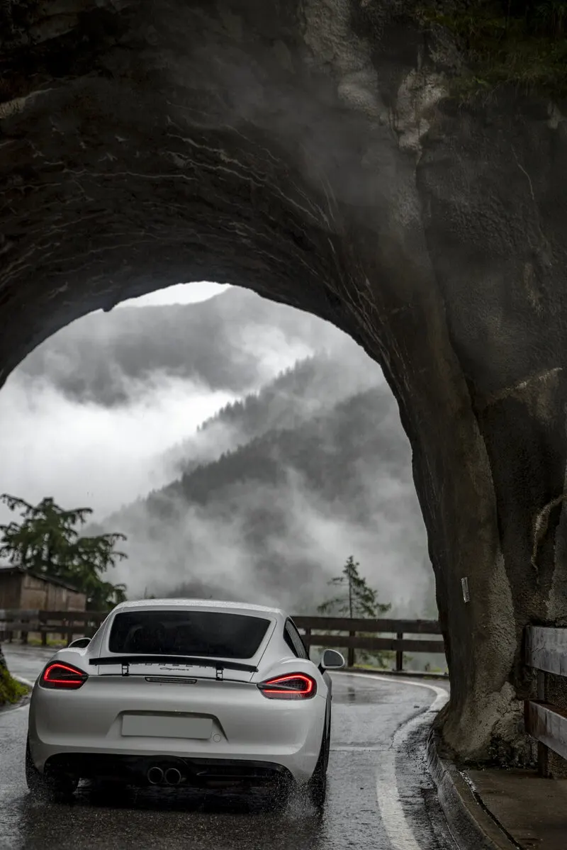 Porsche Cayman auf einer Alpenpassstraße, Blick durch einen Tunnel ins Tal